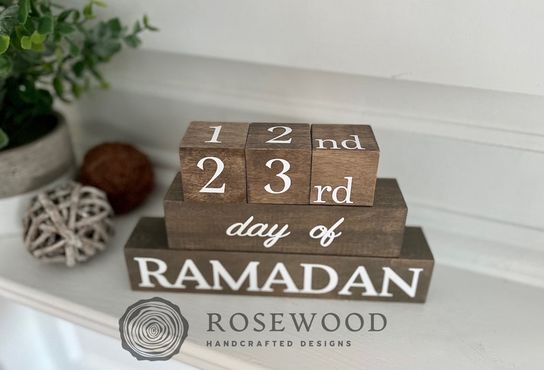 May include: Wooden Ramadan countdown blocks. The blocks are brown with white lettering. The top blocks display the numbers 1, 2, and 3, with "nd" and "rd" on the adjacent blocks. The bottom block reads "day of RAMADAN".