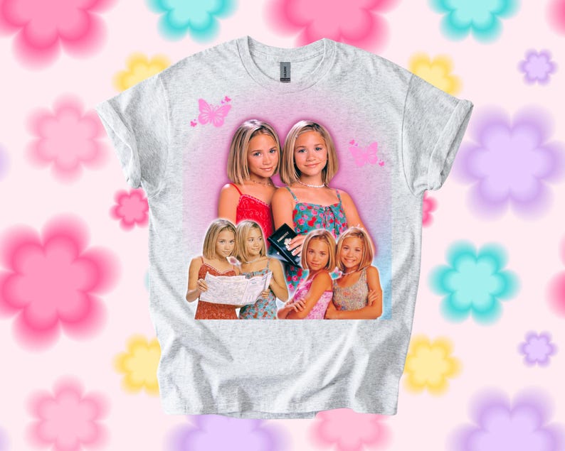 Pu&ograve; includere: T-shirt grigio chiaro con una grafica di due donne. La grafica ha uno sfondo rosa con farfalle e pi&ugrave; immagini delle donne. La t-shirt &egrave; uno stile girocollo.