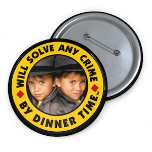 May include: A round pin-back button featuring a yellow border with the black text "WILL SOLVE ANY CRIME BY DINNER TIME" and two red diamond icons. The center displays a photograph of two children wearing grey fedoras and trench coats.