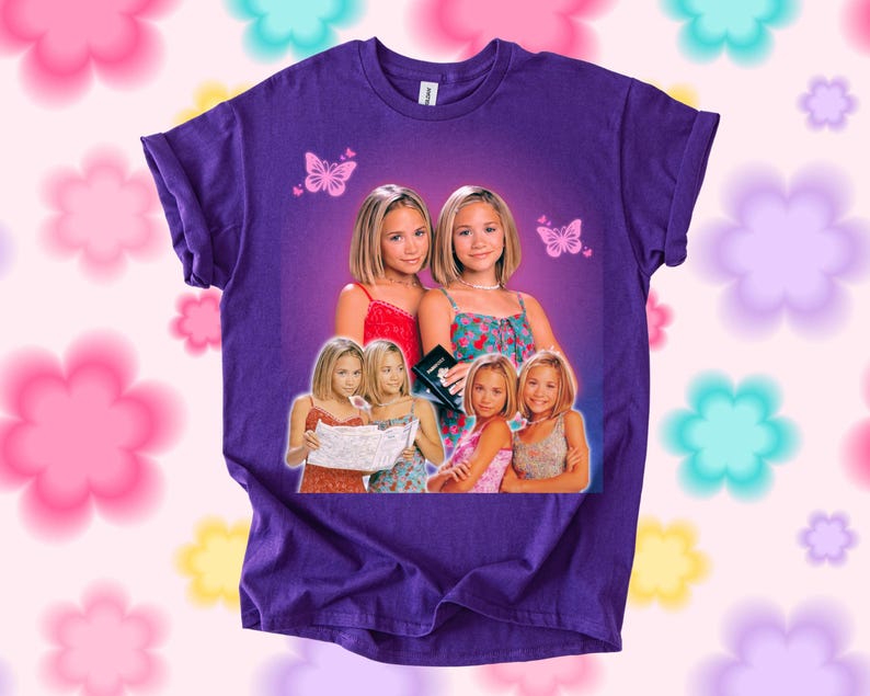 Pu&ograve; includere: T-shirt viola con una grafica di due donne bionde con top colorati. La grafica include farfalle e immagini aggiuntive delle donne. Girocollo.