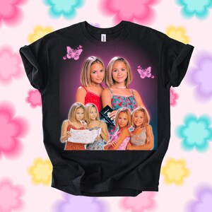 Pu&ograve; includere: T-shirt nero con una grafica di due donne e farfalle. La grafica include pi&ugrave; immagini delle donne in diversi outfit. Lo sfondo &egrave; una sfumatura di viola e rosa.