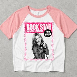May include: A white and pink raglan t-shirt featuring a black and white photograph of a person holding a microphone. The graphic includes the text ROCK STAR, SMART AS CAN BE!, and stuff by duff, all framed by a pink scribbled border design.