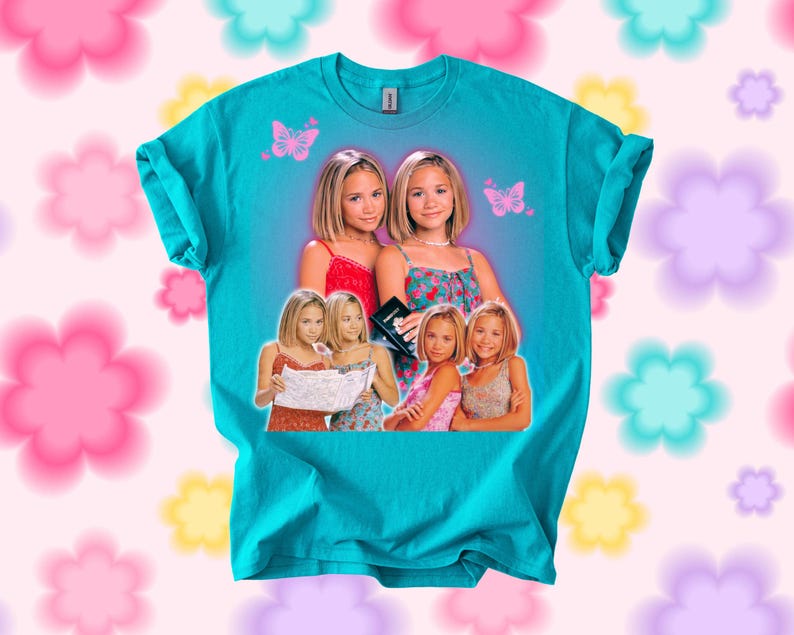 Pu&ograve; includere: T-shirt color turchese con una grafica di due donne, con immagini pi&ugrave; piccole delle stesse donne. Sullo sfondo ci sono farfalle rosa. La maglietta &egrave; del marchio Gildan.
