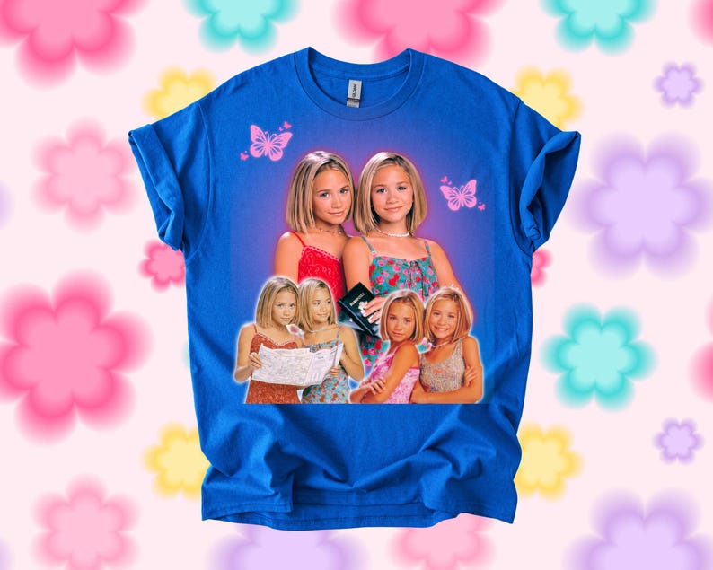 Pu&ograve; includere: T-shirt blu reale con una grafica di due giovani donne, con farfalle. La grafica include pi&ugrave; immagini delle donne in vari outfit. La maglietta &egrave; del marchio Gildan.
