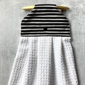 May include: Black and white striped fabric kitchen towel holder with a white terry cloth towel attached. The holder has a button closure and a loop for hanging.