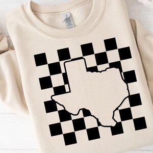 Peut inclure: Un sweat-shirt beige avec un motif à carreaux noir et blanc et un contour blanc de l'état du Texas.