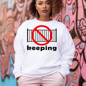 May include: White sweatshirt with a red circle and a black fence with a diagonal red line through it. The text "keeping" is below the circle.