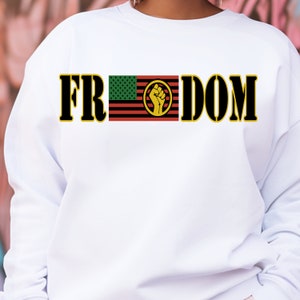 May include: White sweatshirt with the word "FREEDOM" in black block letters with a yellow outline. The "E" is replaced by a flag design with a green star field, red and black stripes, and a yellow fist.