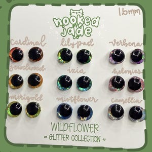 May include: A display card featuring a collection of 16mm glitter eyes from the "Wildflower Glitter Collection." The eyes are in various colors, including red, green, purple, and blue, with names like "Cardinal," "Lilypad," and "Verbena."