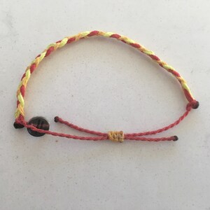 Könnte beinhalten: Ein geflochtenes Freundschaftsarmband in Rot und Gelb mit einem silbernen Verschluss.