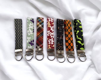 May include: Seven colorful keychains with different patterns, including plaid, floral, and geometric designs. Each keychain has a silver key ring.