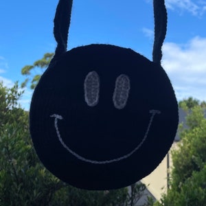 May include: A black crocheted bag with a white smiley face design. The bag has two long straps.