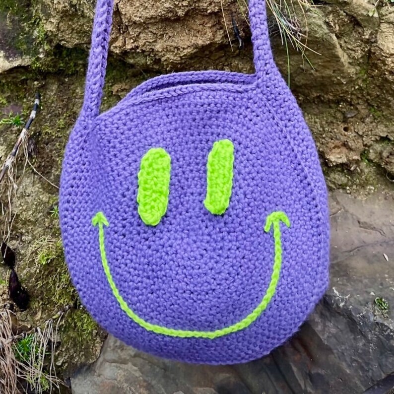 May include: Purple crocheted tote bag with a green smiley face design.