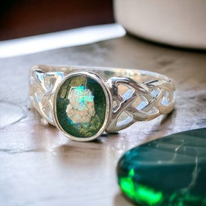 May include: A silver ring with a Celtic knot design and a green and iridescent oval stone.