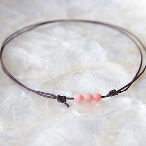 May include: A simple necklace with a brown cord and three pink beads.