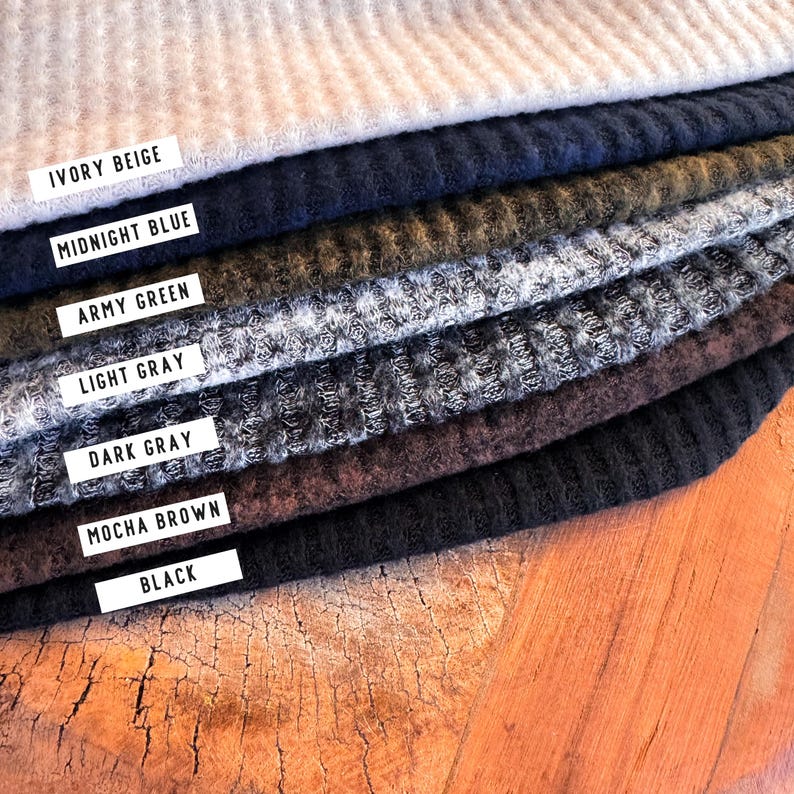 May include: A selection of fabric swatches in shades such as ivory beige, midnight blue, army green, light grey, dark grey, mocha brown, and black. Each colour is identified with a white label. The fabric has a textured, ribbed design.