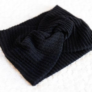 May include: A black, textured headband with a knotted design. The headband is made of a soft, ribbed fabric. This accessory is perfect for keeping hair out of the face.