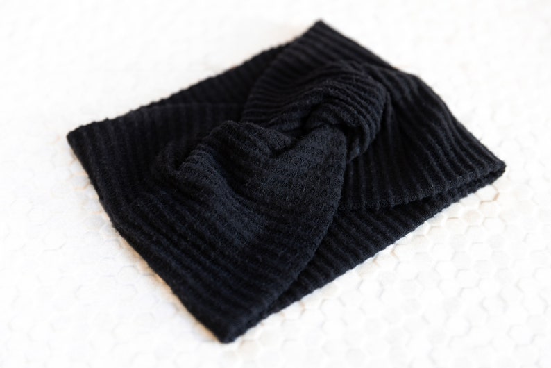 May include: A black, textured headband with a knotted design. The headband is made of a soft, ribbed fabric. This accessory is perfect for keeping hair out of the face.