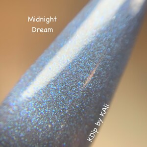 May include: Close-up of a nail with a shimmering, iridescent finish in shades of blue and silver. The text "Midnight Dream" is visible. The nail has a pointed shape and a glossy texture.