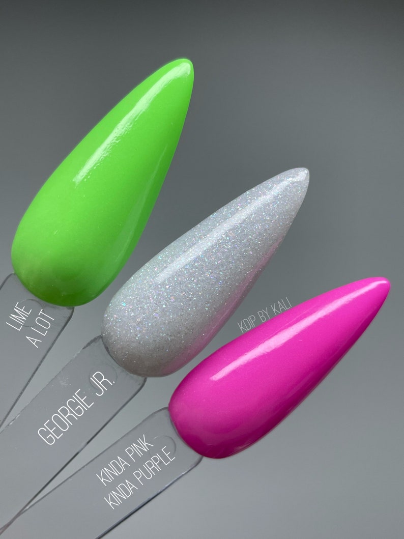 May include: Three nail polish bottles with different colors and names. The first bottle is green and labeled "Lime A Lot". The second bottle is white with glitter and labeled "Georgie Jr.". The third bottle is pink and labeled "Kinda Pink Kinda Purple".