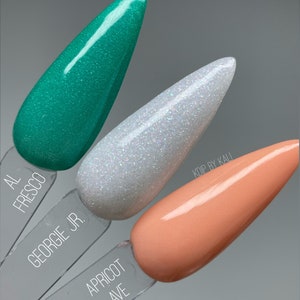 May include: Three nail polish colors in small bottles, from left to right: teal green, white with iridescent glitter, and peach. The bottles are labeled "Al Fresco", "Georgie Jr.", and "Apricot Ave".