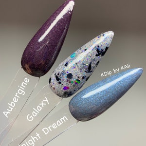 May include: Three nail polish swatches on clear sticks. The colors are Aubergine, Galaxy, and Midnight Dream. Aubergine is a dark purple with glitter. Galaxy is silver with black and iridescent glitter. Midnight Dream is a shimmery blue-gray.