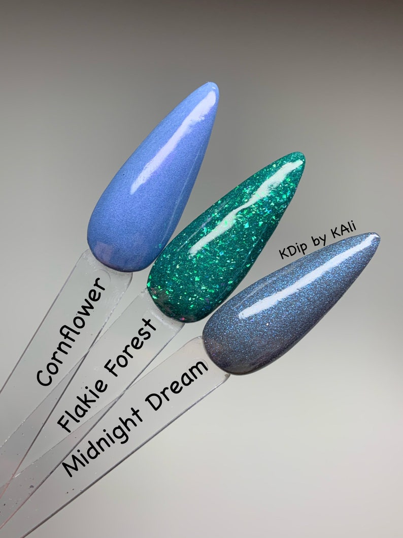 May include: Three nail polish swatches in Cornflower, Flakie Forest, and Midnight Dream. Cornflower is a light blue, Flakie Forest is a glittery teal, and Midnight Dream is a dark blue with shimmer. The text "KDip by KAli" is visible.