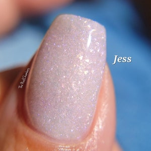 May include: A close-up of a fingernail with a white nail polish with iridescent glitter. The nail polish is called "Jess".
