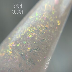 May include: Close-up of a clear bottle with iridescent glitter inside. The bottle is labeled "SPUN SUGAR" and "KODP BY KALI".