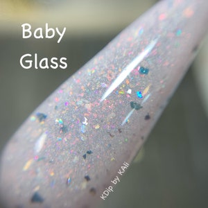 K&ouml;nnte beinhalten: Nahaufnahme einer durchsichtigen Nagellackflasche mit hellrosa Basis und schimmerndem Glitzer. Die Flasche ist mit "KDip by KALI" beschriftet und der Text "Baby Glass" ist oben links sichtbar.