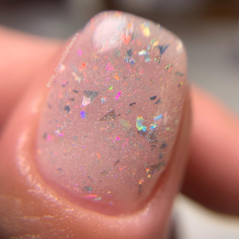 K&ouml;nnte beinhalten: Nahaufnahme eines klaren Nagellacks mit schimmerndem Glitzer. Der Glitzer ist eine Mischung aus Silber, Gold und Regenbogenfarben.