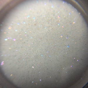 May include: Close-up view of a white, sparkly, iridescent glitter. The glitter is very fine and has a subtle shimmer.