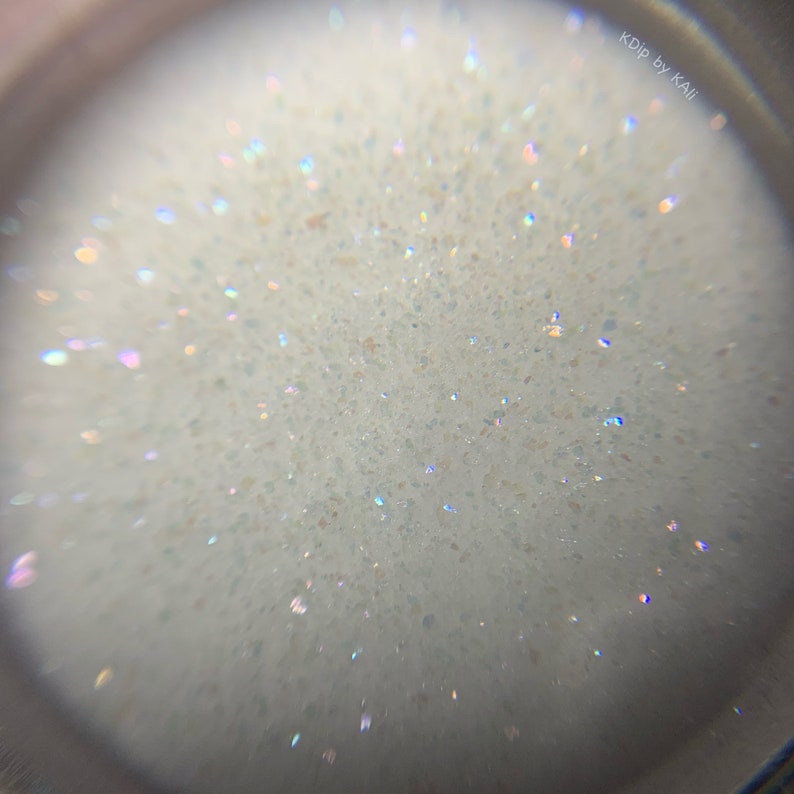 May include: Close-up view of a white, sparkly, iridescent glitter. The glitter is very fine and has a subtle shimmer.