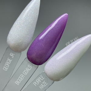 May include: Three nail polish bottles with glitter finish. The bottles are labeled "Georgie Jr.", "Bigger Goals", and "Purple Haze".
