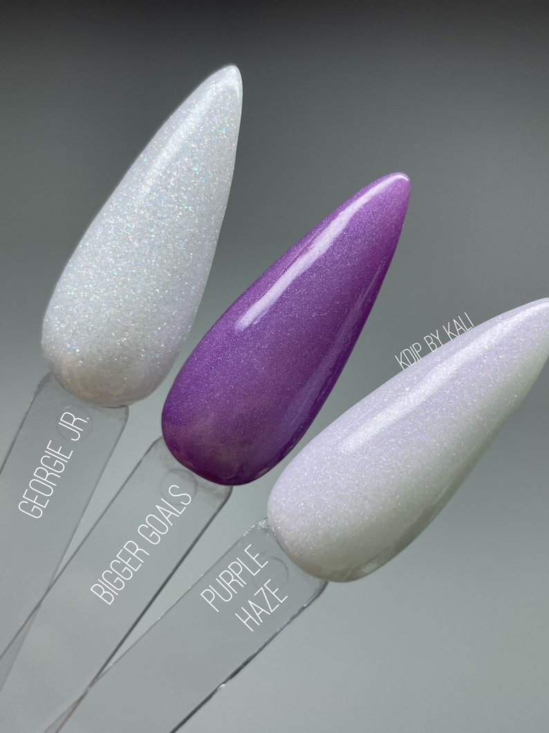 May include: Three nail polish bottles with glitter finish. The bottles are labeled "Georgie Jr.", "Bigger Goals", and "Purple Haze".