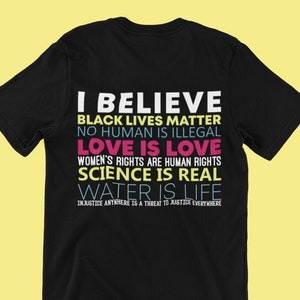 May include: Black t-shirt with a white, pink, and blue graphic print that reads "I Believe Black Lives Matter No Human Is Illegal Love Is Love Women's Rights Are Human Rights Science Is Real Water Is Life Injustice Anywhere Is A Threat To Justice Everywhere"