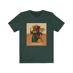 May include: A green t-shirt with a graphic of the Empress tarot card. The Empress is a black woman sitting on a throne with a crown and a scepter. The card is surrounded by a gold frame and the text "THE EMPRESS" is printed below the image.