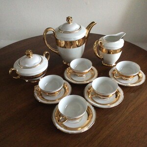 May include: A white porcelain tea set with gold trim. The set includes a teapot, creamer, sugar bowl, and four cups and saucers.