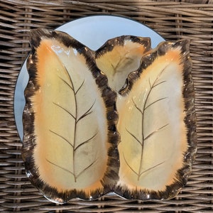 May include: A set of two ceramic leaf-shaped serving dishes with a brown rim and a gold leaf design.