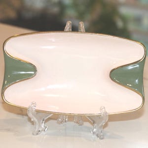 May include: A white and green ceramic serving dish with gold trim. The dish has an hourglass shape with a white centre and green accents on each end. The gold trim adds elegance to this decorative piece.