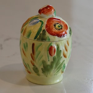 May include: A yellow ceramic jar with a lid, decorated with hand-painted red poppies and green leaves.