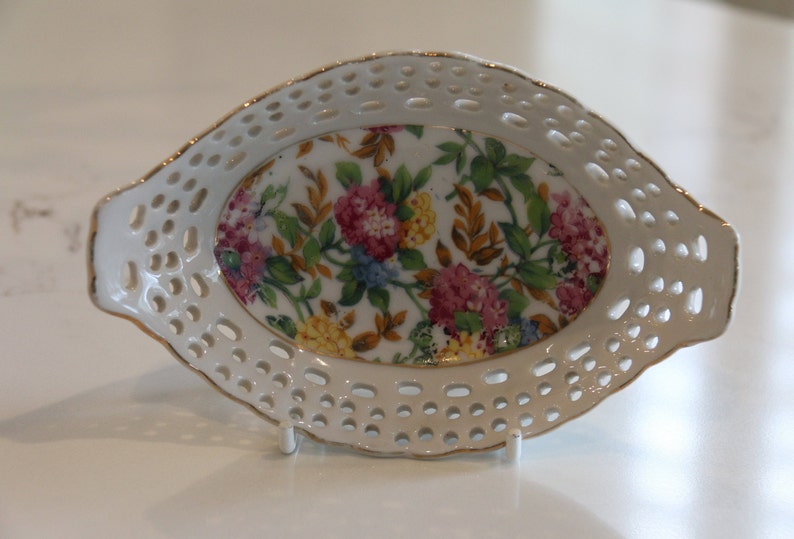 K&ouml;nnte beinhalten: Eine wei&szlig;e ovale Porzellansch&uuml;ssel mit Blumenmuster. Die Sch&uuml;ssel hat einen spitzengleichen Rand und einen goldenen Rand.