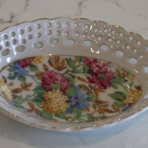 K&ouml;nnte beinhalten: Eine wei&szlig;e Porzellansch&uuml;ssel mit goldfarbenem Rand und einem Blumendesign. Die Sch&uuml;ssel hat einen spitzengleichen Rand und ist perfekt zum Servieren kleiner Snacks oder Leckereien.