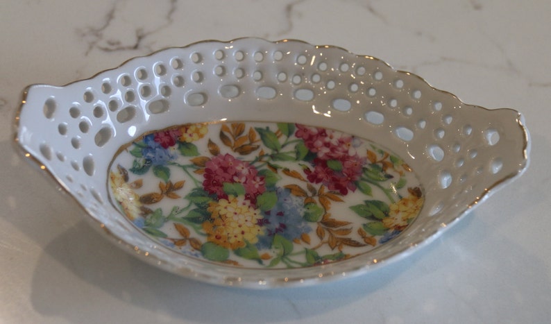 K&ouml;nnte beinhalten: Eine wei&szlig;e Porzellansch&uuml;ssel mit goldfarbenem Rand und einem Blumendesign. Die Sch&uuml;ssel hat einen spitzengleichen Rand und ist perfekt zum Servieren kleiner Snacks oder Leckereien.