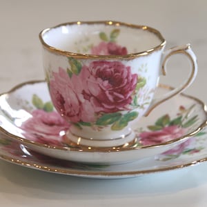 May include: A fine bone china teacup, saucer, and side plate set. The white porcelain is decorated with pink roses and green leaves. The edges are trimmed with gold. The set is ideal for afternoon tea.