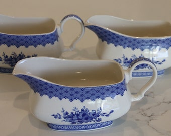 May include: Three white ceramic gravy boats with blue and white floral designs. The boats have a scalloped edge and a handle.