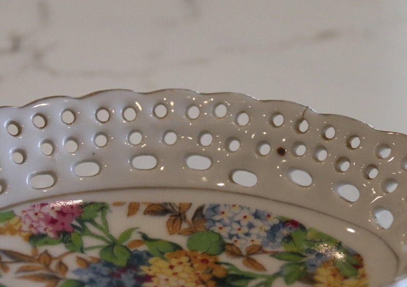 K&ouml;nnte beinhalten: Wei&szlig;e Keramikplatte mit einem gewellten Rand und einem Blumendesign. Die Platte hat ein spitzendes Muster mit kleinen L&ouml;chern am Rand.