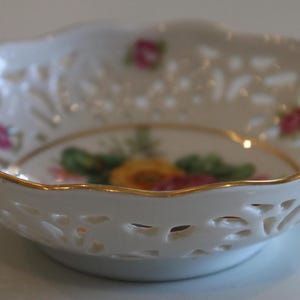 May include: A white porcelain bowl with a gold rim and delicate floral design. The bowl has a lace-like pattern and features a floral motif in the centre.