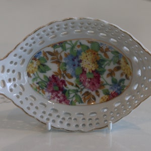 K&ouml;nnte beinhalten: Wei&szlig;e ovale Porzellansch&uuml;ssel mit Blumenmuster und einer spitzengleichen Bord&uuml;re. Die Sch&uuml;ssel hat einen goldenen Rand.
