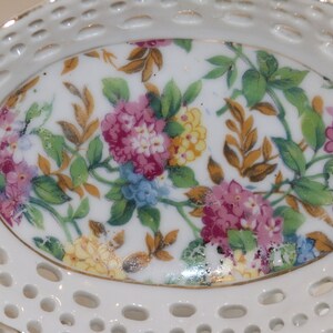 K&ouml;nnte beinhalten: Eine wei&szlig;e Porzellanschale mit einem Blumendesign. Die Schale hat einen gewellten Rand und ein spitzendes Muster um den Rand. Das Blumendesign zeigt rosa, gelbe und blaue Blumen auf wei&szlig;em Hintergrund.